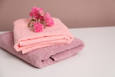 Photo of Stack of colorful towels and flowers on white table, closeup. Space for text