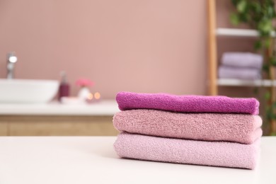 Photo of Stack of colorful towels on white table in bathroom, closeup. Space for text