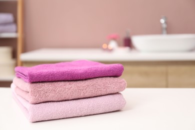 Photo of Stack of colorful towels on white table in bathroom, closeup. Space for text