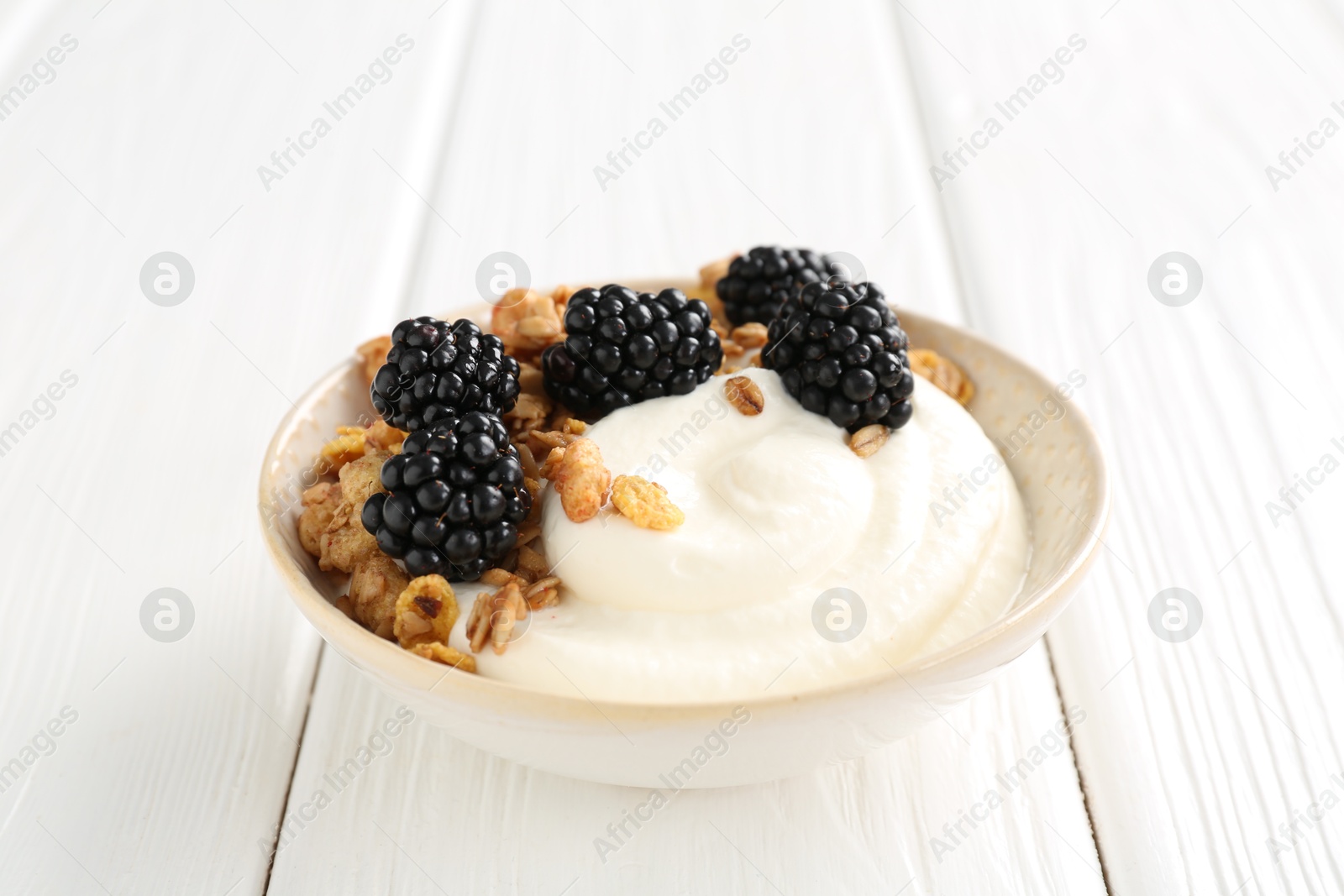 Tasty yogurt with granola and blackberries in bowl on white wooden table, closeup Photo of Tasty yogurt with granola and blackberries in bowl on white wooden table, closeup