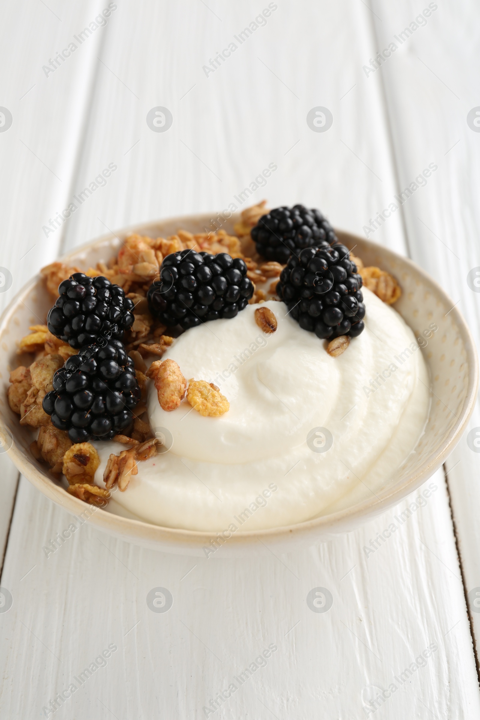 Photo of Tasty yogurt with granola and blackberries in bowl on white wooden table, closeup