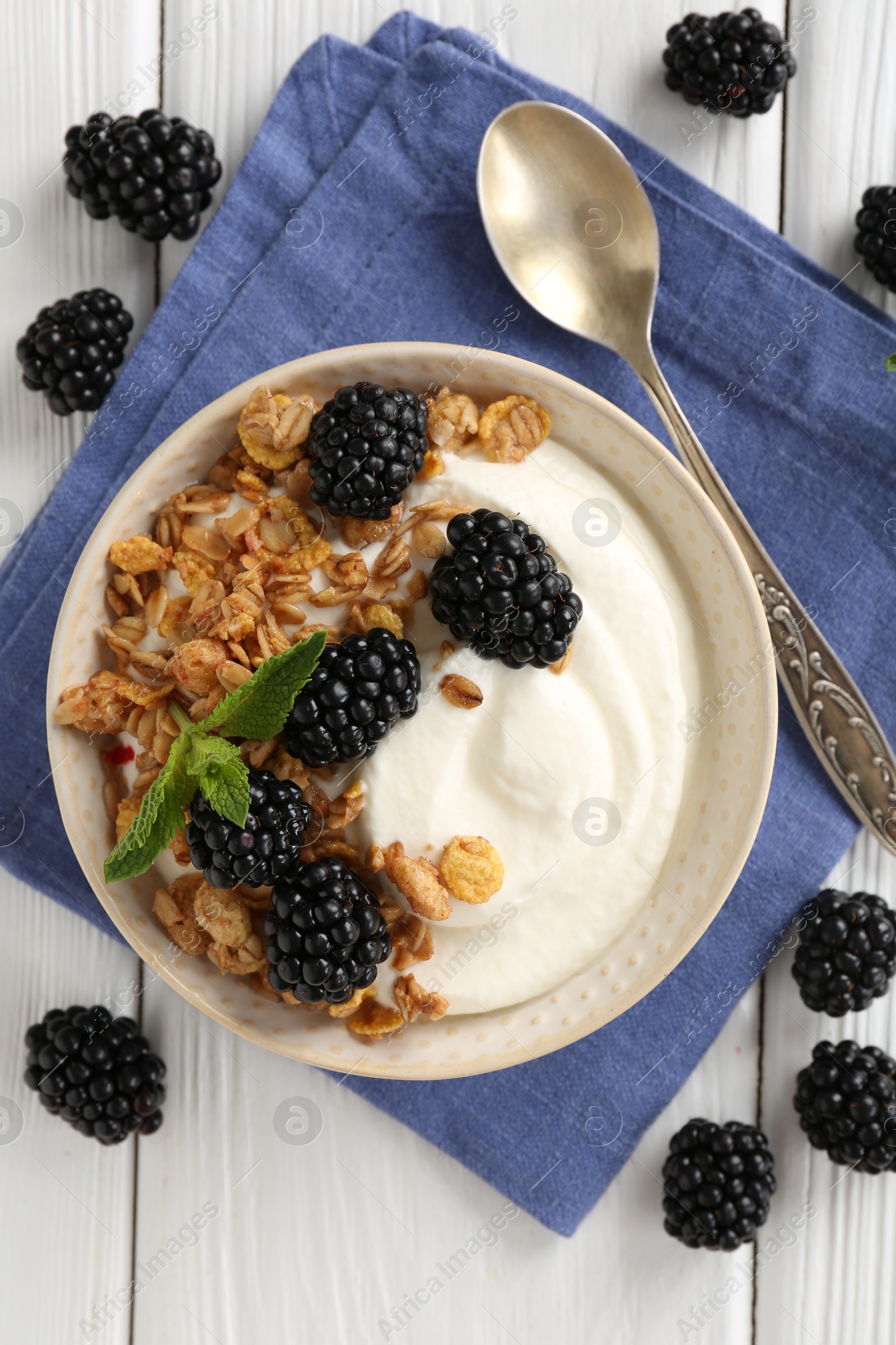 Photo of Tasty yogurt with granola and blackberries in bowl on white wooden table, flat lay