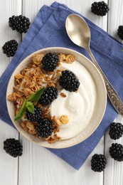 Photo of Tasty yogurt with granola and blackberries in bowl on white wooden table, flat lay