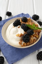Photo of Tasty yogurt with granola and blackberries in bowl on white wooden table, closeup