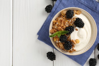Photo of Tasty yogurt with granola and blackberries in bowl on white wooden table, flat lay. Space for text