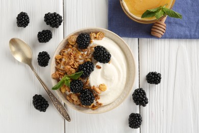 Photo of Tasty yogurt with granola, honey and blackberries in bowl on white wooden table, flat lay