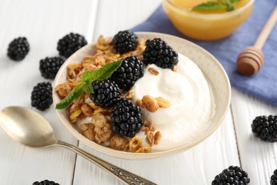 Photo of Tasty yogurt with granola, honey and blackberries in bowl on white wooden table, closeup