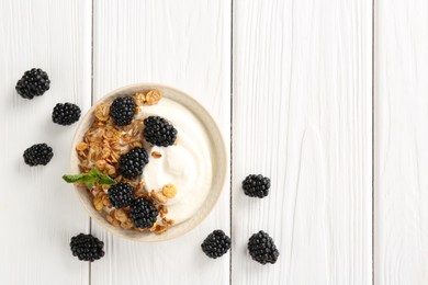 Photo of Tasty yogurt with granola and blackberries in bowl on white wooden table, flat lay. Space for text