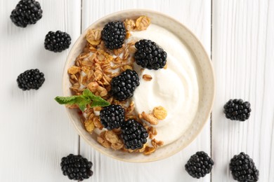 Photo of Tasty yogurt with granola and blackberries in bowl on white wooden table, flat lay