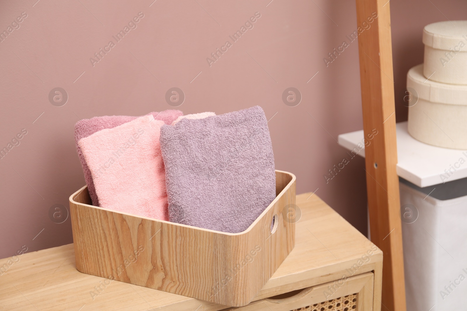 Colorful towels in wooden basket on cabinet indoors Photo of Colorful towels in wooden basket on cabinet indoors