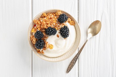 Photo of Tasty yogurt with granola and blackberries in bowl on white wooden table, top view