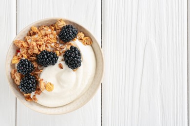 Photo of Tasty yogurt with granola and blackberries in bowl on white wooden table, top view. Space for text