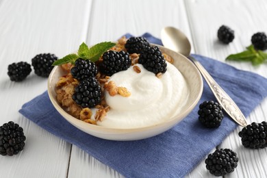 Photo of Tasty yogurt with granola and blackberries in bowl on white wooden table, closeup