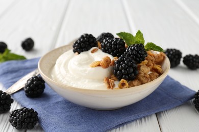 Photo of Tasty yogurt with granola and blackberries in bowl on white wooden table, closeup
