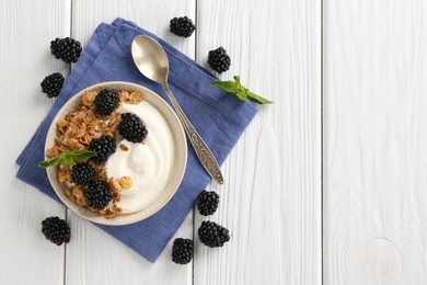 Photo of Tasty yogurt with granola and blackberries in bowl on white wooden table, flat lay. Space for text