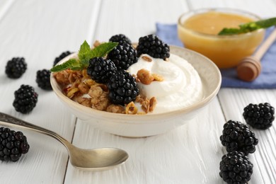 Photo of Tasty yogurt with granola, honey and blackberries in bowl on white wooden table, closeup