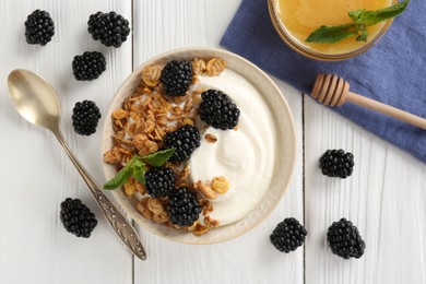 Photo of Tasty yogurt with granola, honey and blackberries in bowl on white wooden table, flat lay