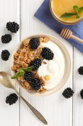 Photo of Tasty yogurt with granola, honey and blackberries in bowl on white wooden table, flat lay