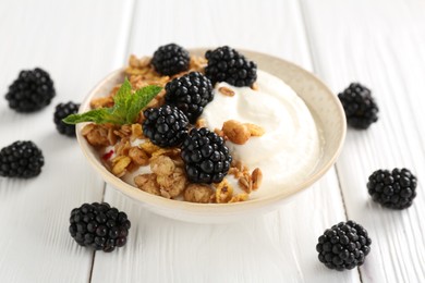 Photo of Tasty yogurt with granola and blackberries in bowl on white wooden table, closeup