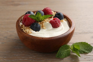 Photo of Tasty yogurt with granola and berries in bowl on wooden table, closeup