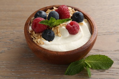 Photo of Tasty yogurt with granola and berries in bowl on wooden table, closeup