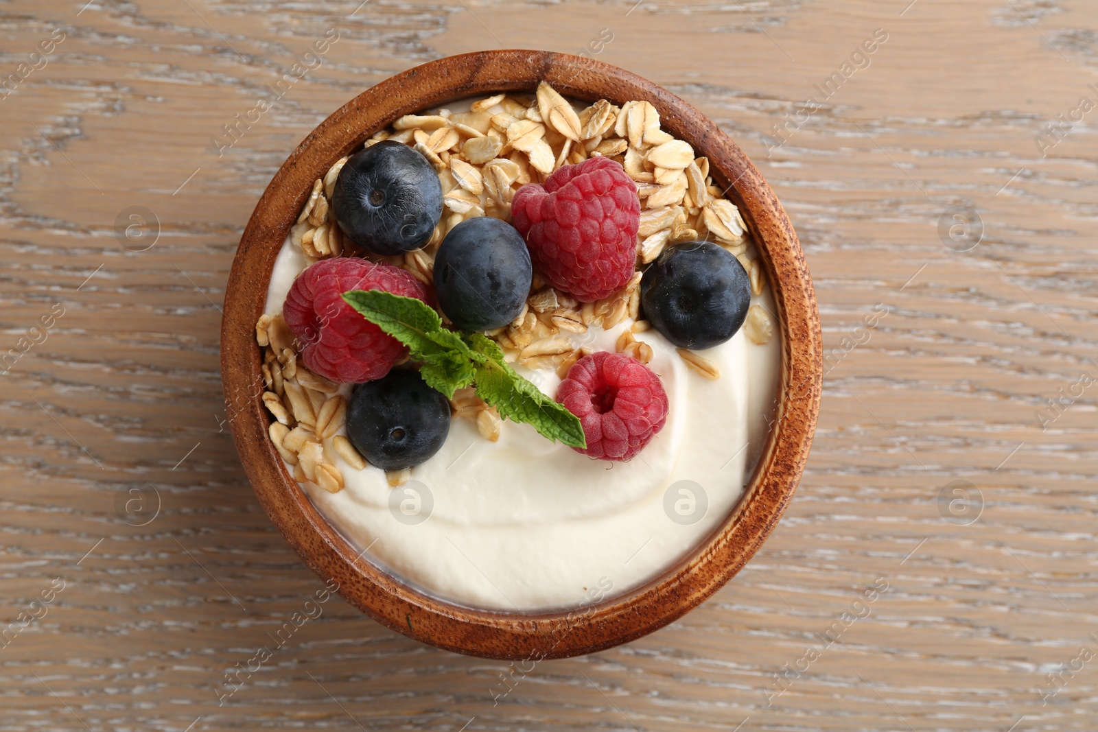 Tasty yogurt with granola and berries in bowl on wooden table, top view Photo of Tasty yogurt with granola and berries in bowl on wooden table, top view