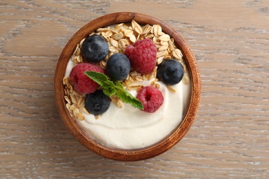 Photo of Tasty yogurt with granola and berries in bowl on wooden table, top view