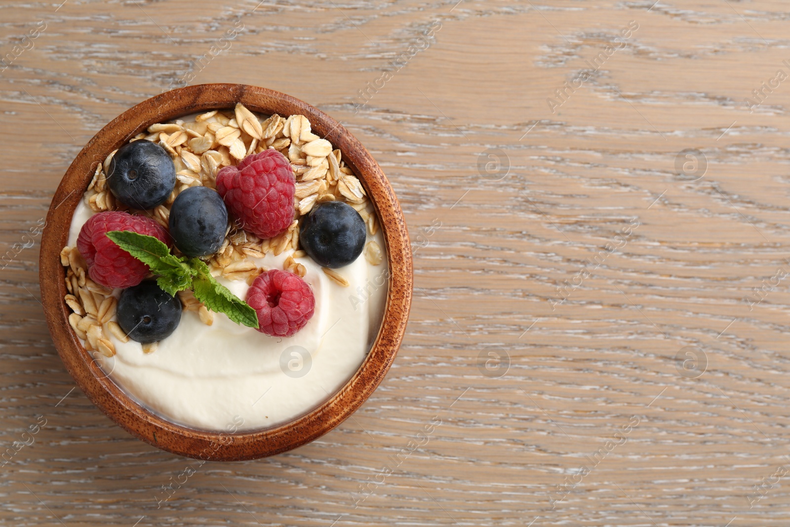 Tasty yogurt with granola and berries in bowl on wooden table, top view. Space for text Photo of Tasty yogurt with granola and berries in bowl on wooden table, top view. Space for text