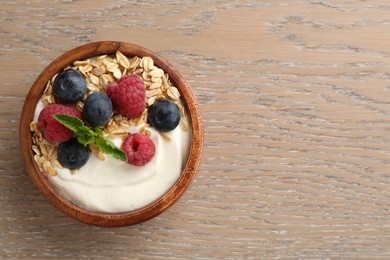 Photo of Tasty yogurt with granola and berries in bowl on wooden table, top view. Space for text