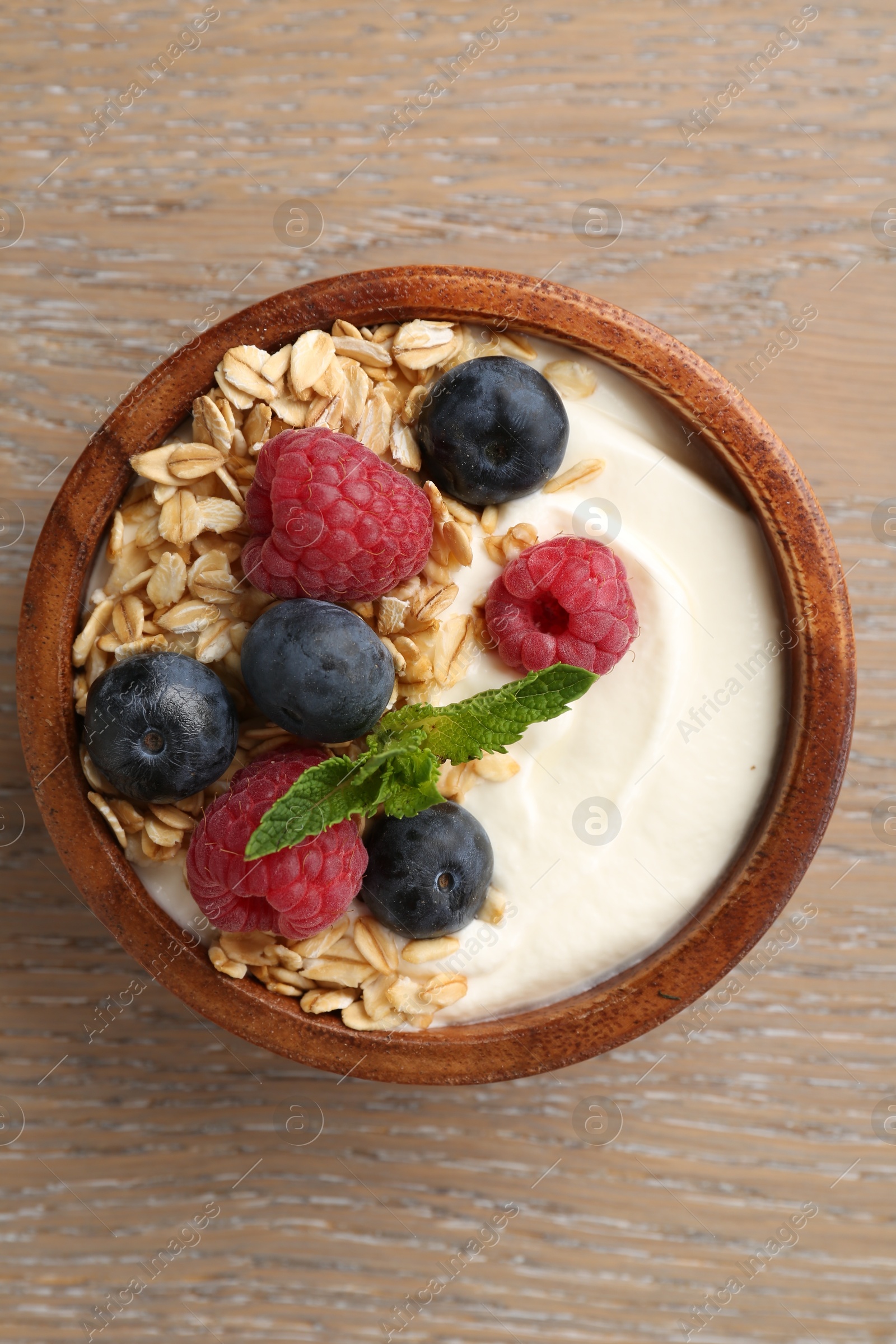 Tasty yogurt with granola and berries in bowl on wooden table, top view Photo of Tasty yogurt with granola and berries in bowl on wooden table, top view