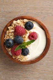 Photo of Tasty yogurt with granola and berries in bowl on wooden table, top view