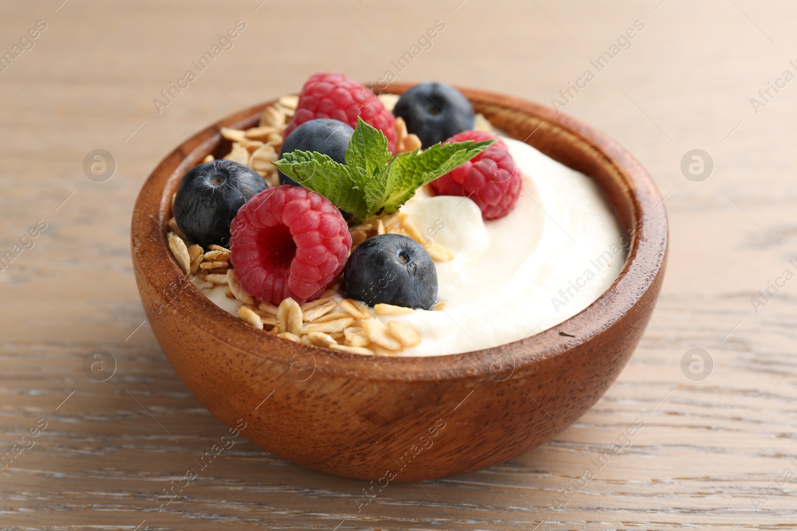Tasty yogurt with granola and berries in bowl on wooden table, closeup Photo of Tasty yogurt with granola and berries in bowl on wooden table, closeup