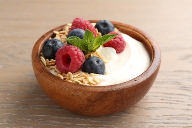 Photo of Tasty yogurt with granola and berries in bowl on wooden table, closeup