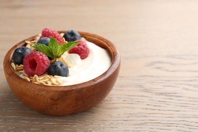 Photo of Tasty yogurt with granola and berries in bowl on wooden table, closeup. Space for text