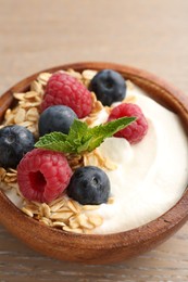 Photo of Tasty yogurt with granola and berries in bowl on wooden table, closeup