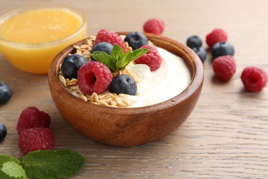 Photo of Tasty yogurt with granola, honey and berries in bowl on wooden table, closeup