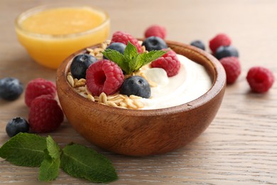Photo of Tasty yogurt with granola, honey and berries in bowl on wooden table, closeup