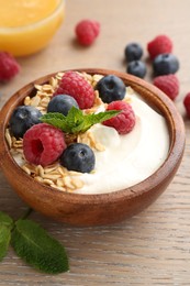 Photo of Tasty yogurt with granola, honey and berries in bowl on wooden table, closeup