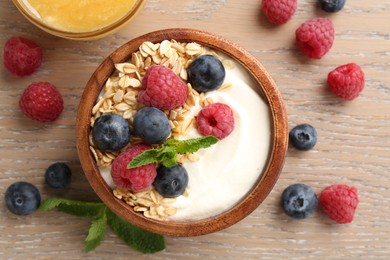 Photo of Tasty yogurt with granola, honey and berries in bowl on wooden table, flat lay