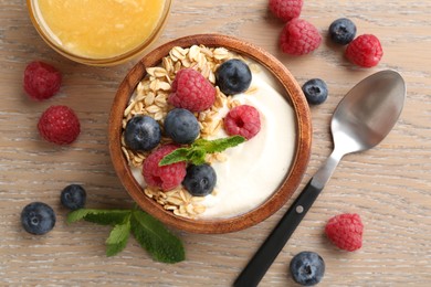 Photo of Tasty yogurt with granola, honey and berries in bowl on wooden table, flat lay