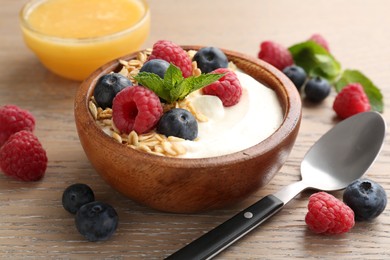 Photo of Tasty yogurt with granola, honey and berries in bowl on wooden table, closeup