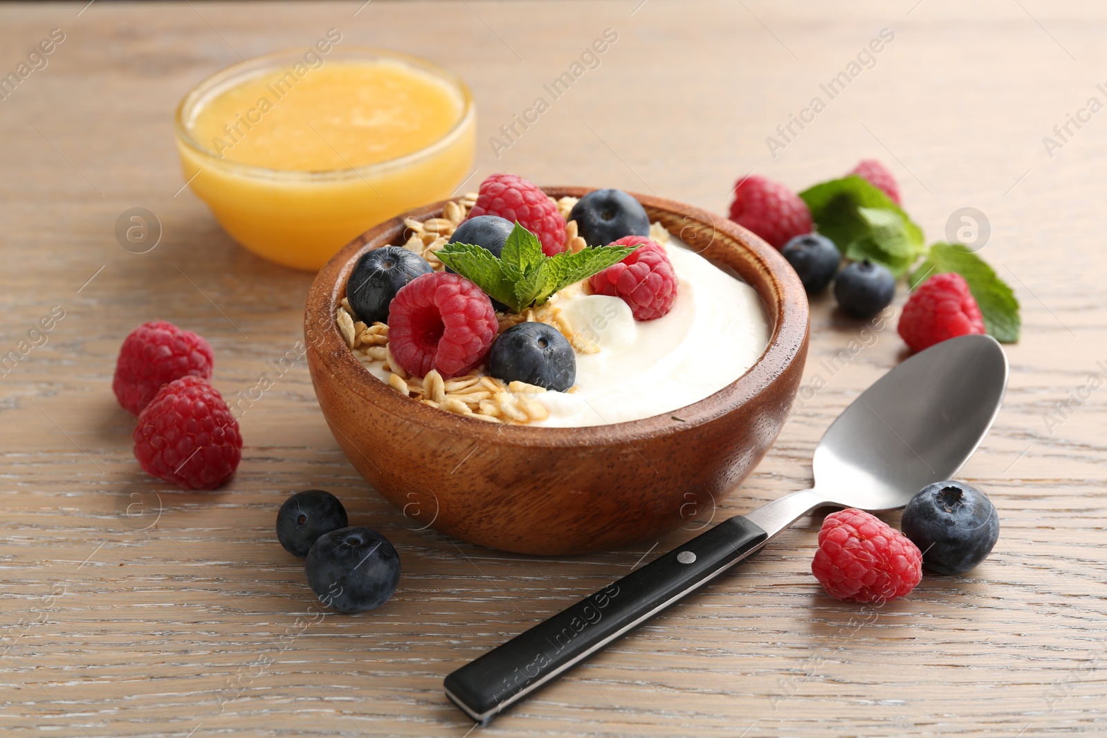 Tasty yogurt with granola, honey and berries in bowl on wooden table, closeup Photo of Tasty yogurt with granola, honey and berries in bowl on wooden table, closeup
