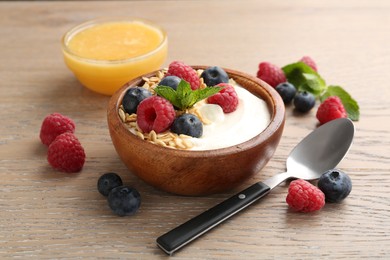 Photo of Tasty yogurt with granola, honey and berries in bowl on wooden table, closeup