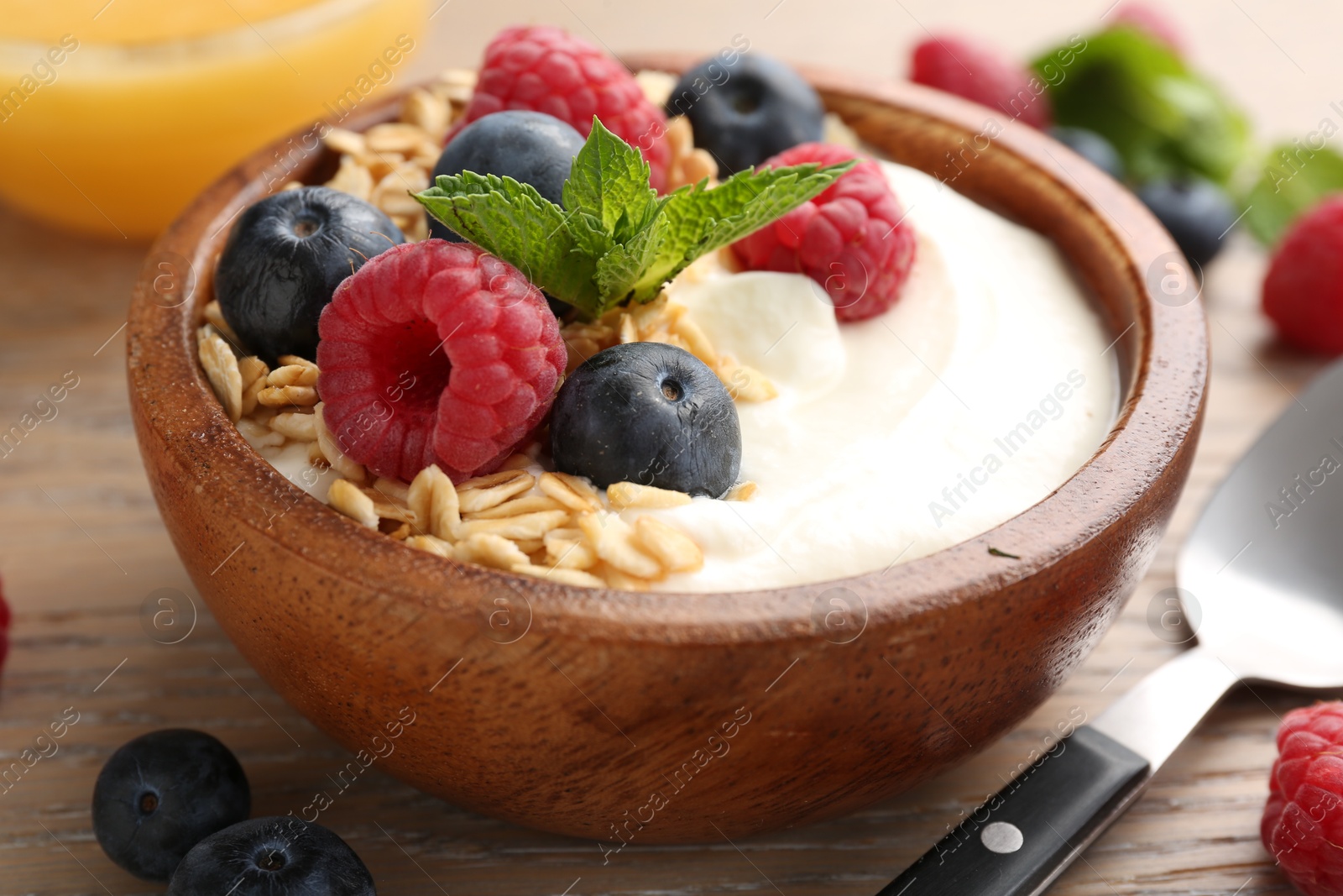 Tasty yogurt with granola and berries in bowl on wooden table, closeup Photo of Tasty yogurt with granola and berries in bowl on wooden table, closeup
