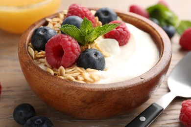 Photo of Tasty yogurt with granola and berries in bowl on wooden table, closeup