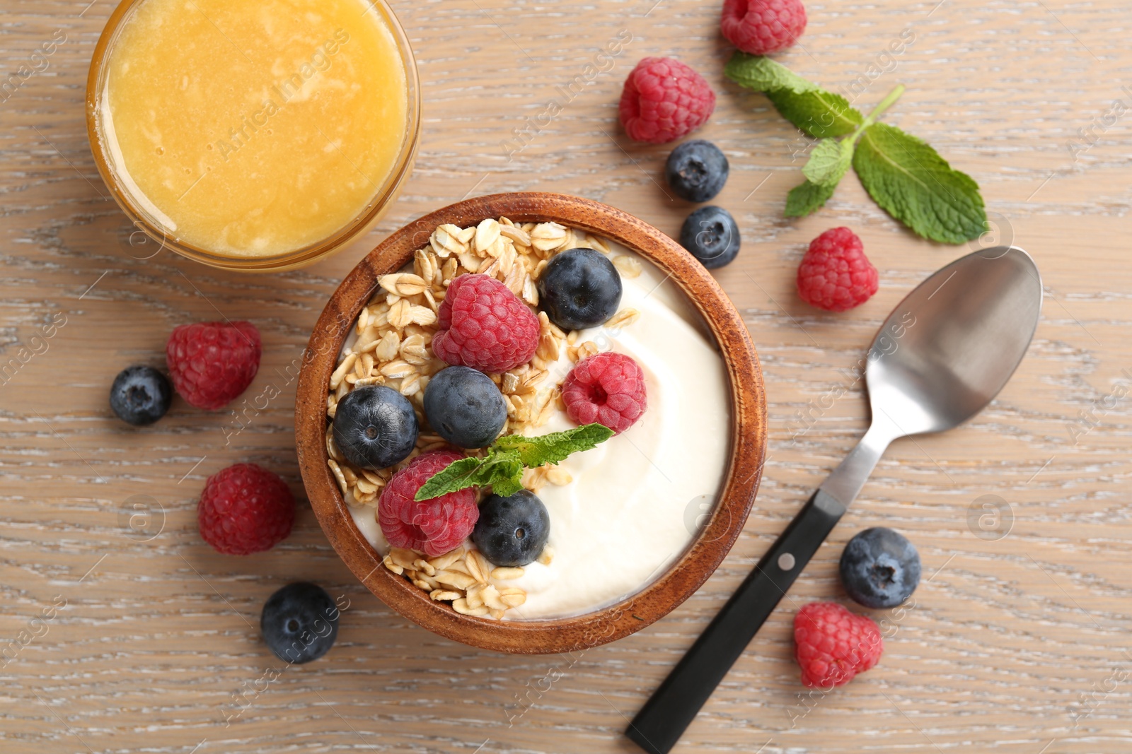 Tasty yogurt with granola, honey and berries in bowl on wooden table, flat lay Photo of Tasty yogurt with granola, honey and berries in bowl on wooden table, flat lay