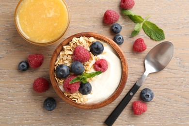 Photo of Tasty yogurt with granola, honey and berries in bowl on wooden table, flat lay