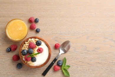 Photo of Tasty yogurt with granola, honey and berries in bowl on wooden table, flat lay. Space for text