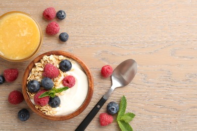 Photo of Tasty yogurt with granola, honey and berries in bowl on wooden table, flat lay. Space for text