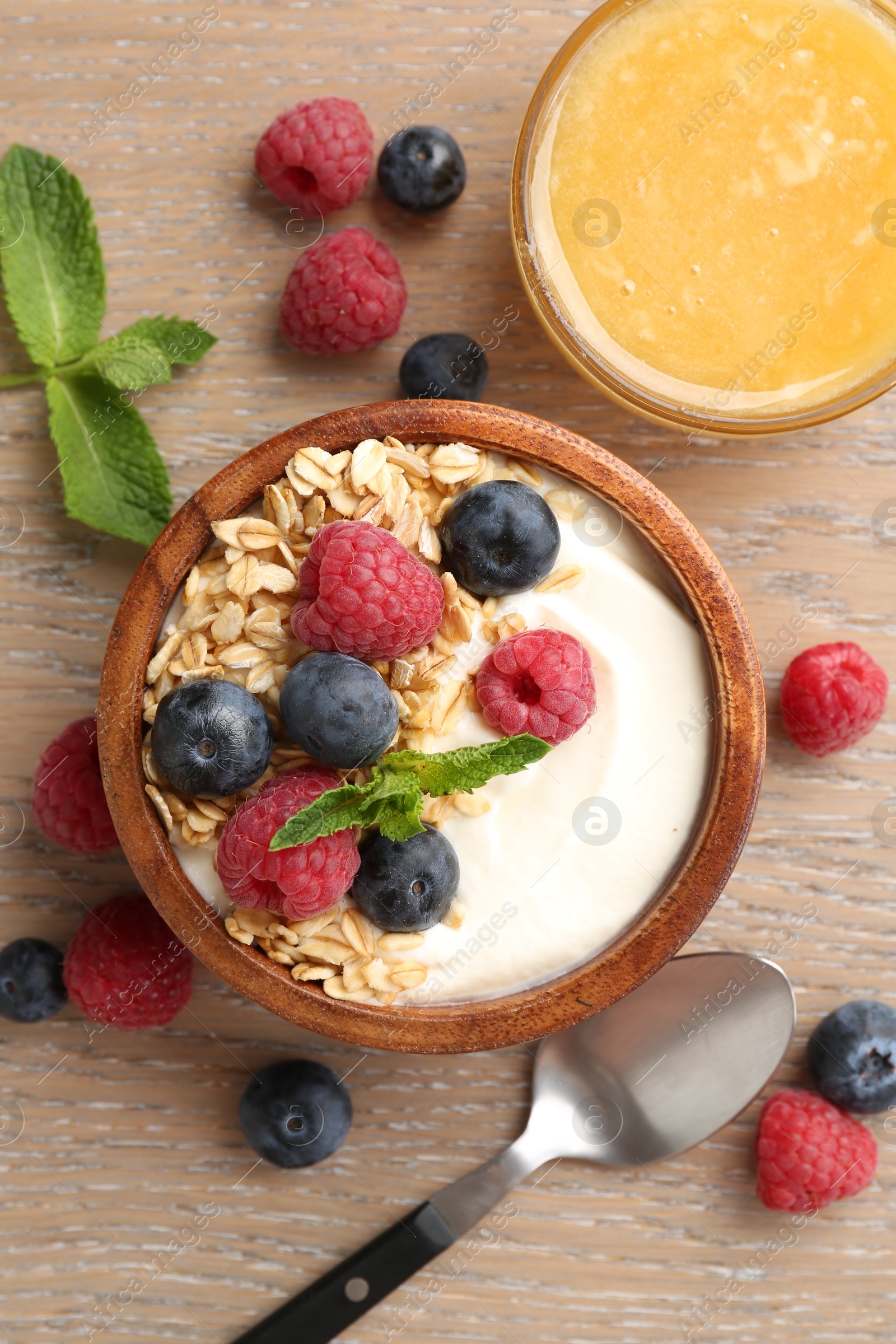 Tasty yogurt with granola, honey and berries in bowl on wooden table, flat lay Photo of Tasty yogurt with granola, honey and berries in bowl on wooden table, flat lay